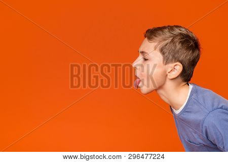 Little Boy Teasing Someone, Showing Tongue And Making Face At Free Space Aside, Orange Background