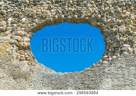 A Hole In The Stone Wall And The Blue Sky In The Background, A Ruined Wall With A Hole. The Image Ca