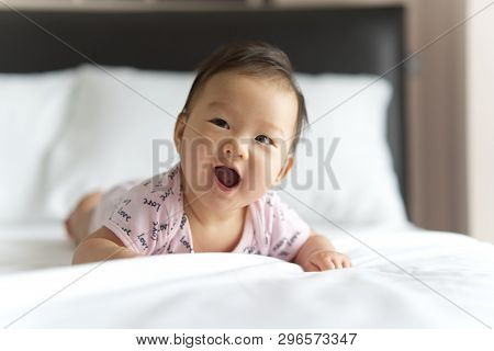 Young Cute Asian Baby Crawling On Bed In Bedroom. The Baby Is Smiling And Looking At The Right With