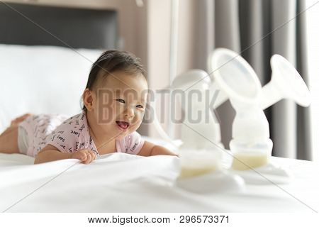 Breast Milk In Milk Pump's Bottles On The Bed With Selective Focus On Smiling Crawling Baby. The Mil