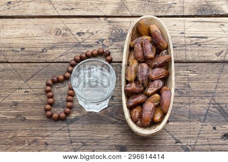 Dried Dates Fruits On A Branch And A Glass Of Water On A Wooden Table. Traditional Fast Breaking, Mu