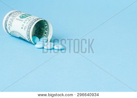 Money Dollar Rolled Up With Pills Flowing Out Isolated On Blue Background, High Costs Of Expensive M