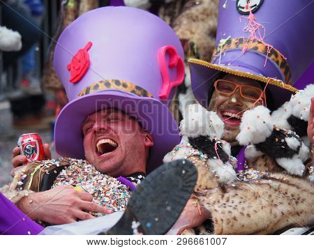 Aalst, Belgium - February 27 2017: Two Men Lying In A Wheelbarrow With A Purple Hat On Their Head An