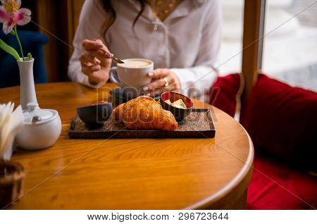 Cappuccino And Frensh Croissant In The Cafe. A Woman Eats Her Breakfast. Wooden Background.