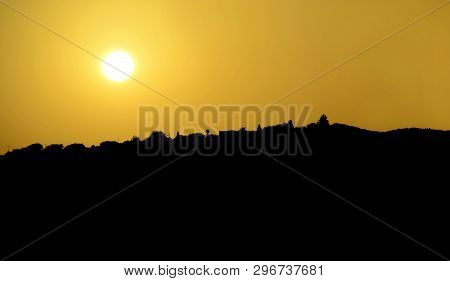 Scenic Landscape In Black And Yellow Colors. Sun In Yellow Sky And Hill Silhouette With Trees At Sun