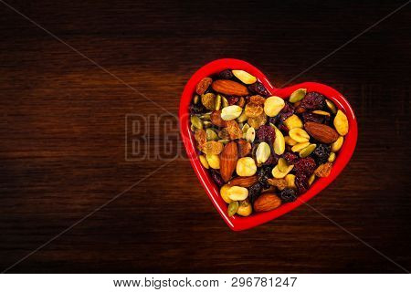 Energy Blend Trail Mix With Nuts And Dried Fruits In Heart Shaped Bowl On Wooden Background. Selecti