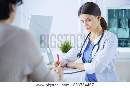 Doctor and patient discussing medical problems in a hospital consulting room. Doc filling in a patient's form