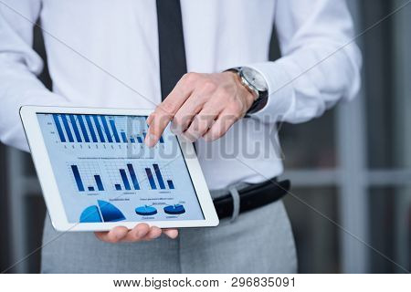 Hand of young elegant economist or analyst in formalwear pointing at financial chart in tablet while making presentation