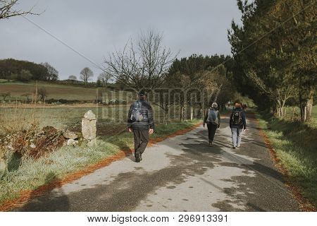 Sarria, Spain - April 7th, 2019: Camino De Santiago Pilgrims Walking With A Backpack Across A Rural 