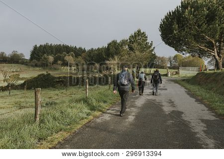 Sarria, Spain - April 6th, 2019: Camino De Santiago Pilgrims Walking With A Backpack Across A Rural 