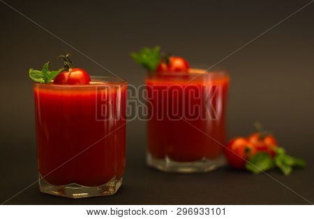 Two glasses of tomato juice with cherry tomatoes and mint with a black background