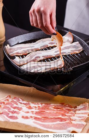 Young Woman In A Gray Apron Fries Bacon