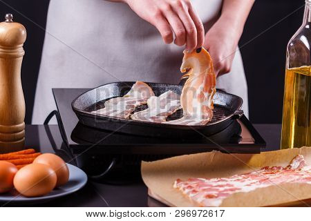 Young Woman In A Gray Apron Fries Bacon