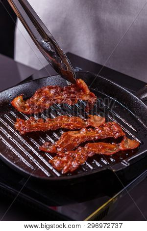 Young Woman In A Gray Apron Fries Bacon