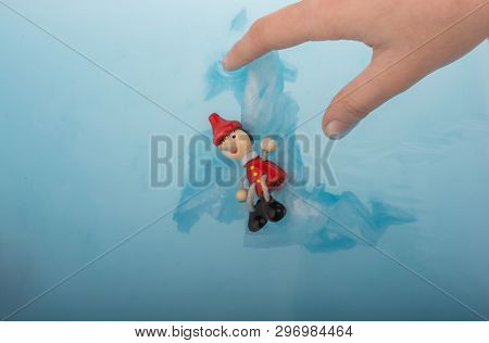 Hand Holding Wodden Puppet Pinocchio On In Blue Water