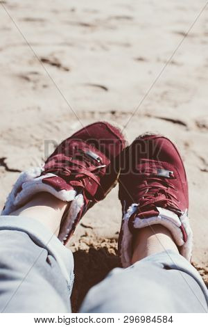 Feet Of Young Woman In Sport Footwear And Jeans Relaxing After Hiking On Sand Beach. Pov. Adventure 