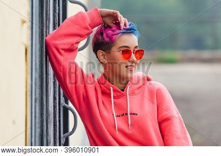 Portrait Of A Young Girl With Short Colorful Hair And Nose Piercing Satanding Near The Wall With Woo