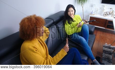 Asian And African American Woman Watching Tv And Eating Chocolate. Emotional Strees Eating Disorder,