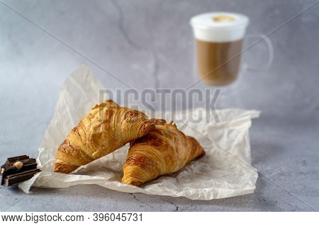 On A Gray Table There Is A Glass Cup With Hot Latte Coffee And Next To It.two Croissants Lie On A Gr