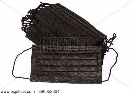 Black Disposable Protective Three-ply Medical Face Mask Against The Stack Of The Same Masks On A Whi