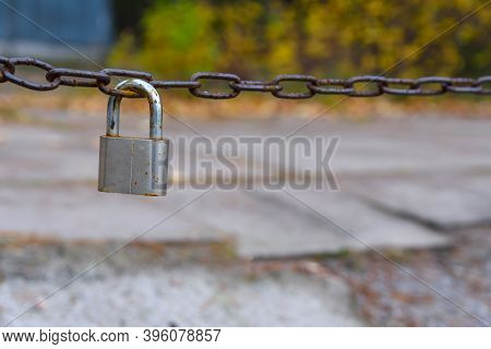 Old And Worn Chrome Padlock Hangs On The Rusty Chain. Chain Protects The Entrance To The Boat Statio