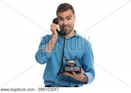 sexy casual man talking on an retro telephone and feeling happily surprised against white background