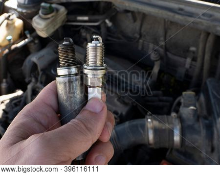 Man Holding old and new car spark plugs on engine background