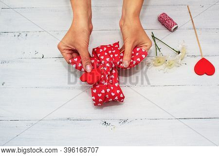 Womens Hands Wrappes Gift Of Valentines Day, Birthday, Mothers Day With Red Textile And Flowers On W