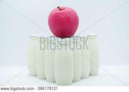 Natural Yogurt With Probiotics And Lactobacillus In Small Plastic Bottles And Red Apple On White Bac
