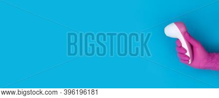 Hand In Pink Medical Glove Holds Pyrometer On Blue Background With Copy Space.