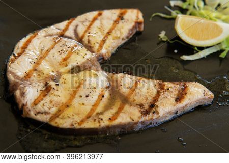 Cooked swordfish. Grilled slice of fish with lemon and salsd on plate in restaurant
