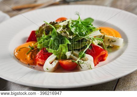 Roasted pepper salad with calamari and fresh greens. Rustic wooden table and grey textile
