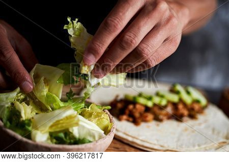 closeup of a young caucasian man preparing a durum or a burrito, with chicken meat cooked with different vegetables such as onion or red and green pepper, and fresh lettuce