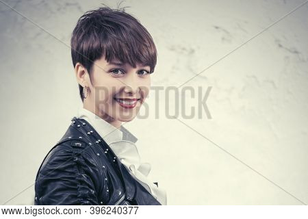 Happy young fashion woman walking on city street Stylish female model in black leather jacket with pixie hair style