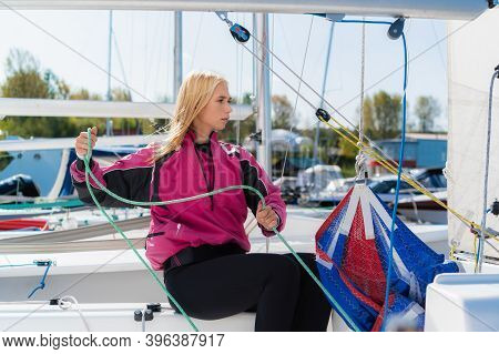 Womens River Regatta On A Sunny Day. A Young Blonde Sets Up The Rigging And Secures The Genaker Sail