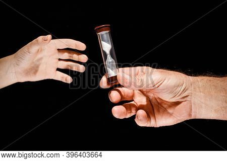 Adalt Hand Passes The Glass Hourglass To The Child Concept Of The Generation Change On A Black Isola