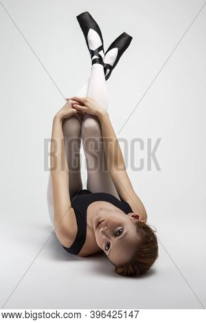 Portrait Of Caucasian Ballet Dancer In Body Suit And Pointes Shoes Lying On Back Against White Backg