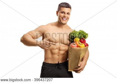 Handsome musuclar young man smiling and pointing at a bag of groceries isolated on white background