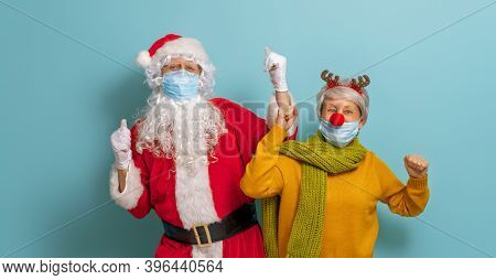 Merry Christmas and Happy Holidays! Santa Claus and reindeer on bright color background. Senior people in carnival costumes wearing face masks during Covid-2019