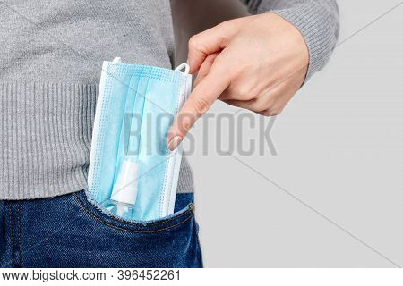 Hand With Medicine Protective Mask And Anticeptic In Jeans Pocket On Grey Background.