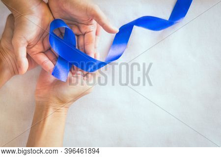 Hands Holding Deep Blue Ribbon On White Fabric With Copy Space. Colorectal Cancer Awareness, Colon C