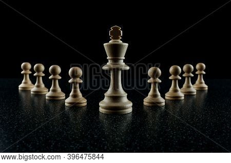 Chess King With A Retinue Of Pawns On A Black Background. The Concept Of A Leader And His Followers.