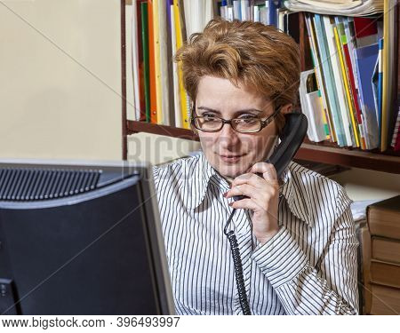 Portrait Of A Busy Woman On The Phone Teleworking At Her Desk At The Home. Working At Home Became An