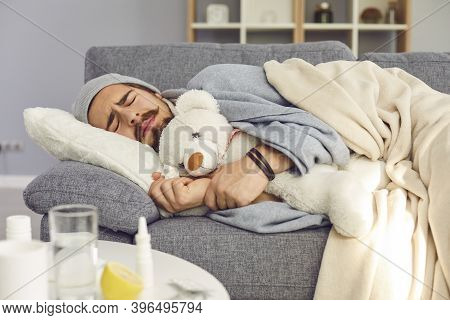 Young Unhappy Man In Warm Clothes Sleeping Under Blanket With Toy And Feeling Cold