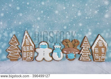 Christmas Ginger Cookies In Protective Masks Among Gingerbread Houses And Fir Trees. Concept Of Wint