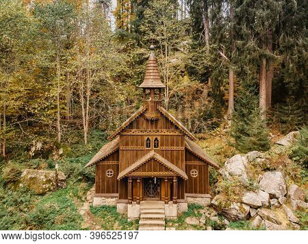 Wooden Pilgrimage Rural Chapel Of Virgin Mary, Cz: Stozecka Kaple, And Iron Cross Standing In Forest