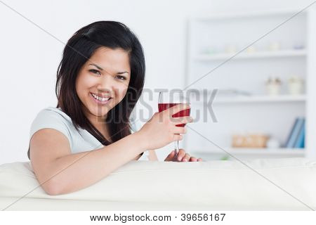 Donna tenendo un bicchiere di vino rosso con una mano mentre il braccio a riposo su un divano in salotto