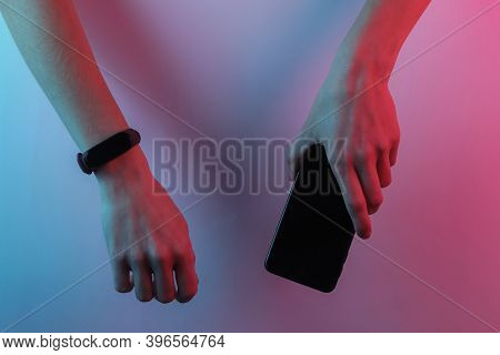 Female Hand With Smart Bracelet And Smartphone. Modern Gadgets. Creative Pop Art Pink Blue Neon Colo