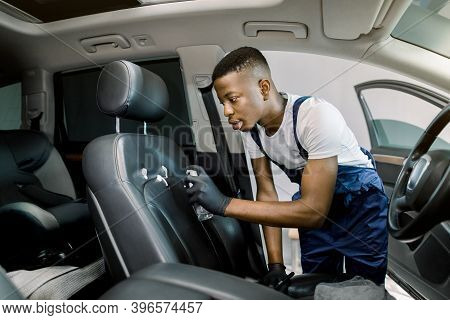 Side View Of Young African Man, Car Service Worker, Wearing Overalls And Protective Gloves, Cleaning