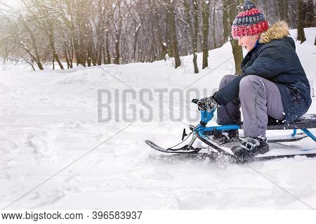 Boy Sledging In A City Park In A Winter Snowy Day.